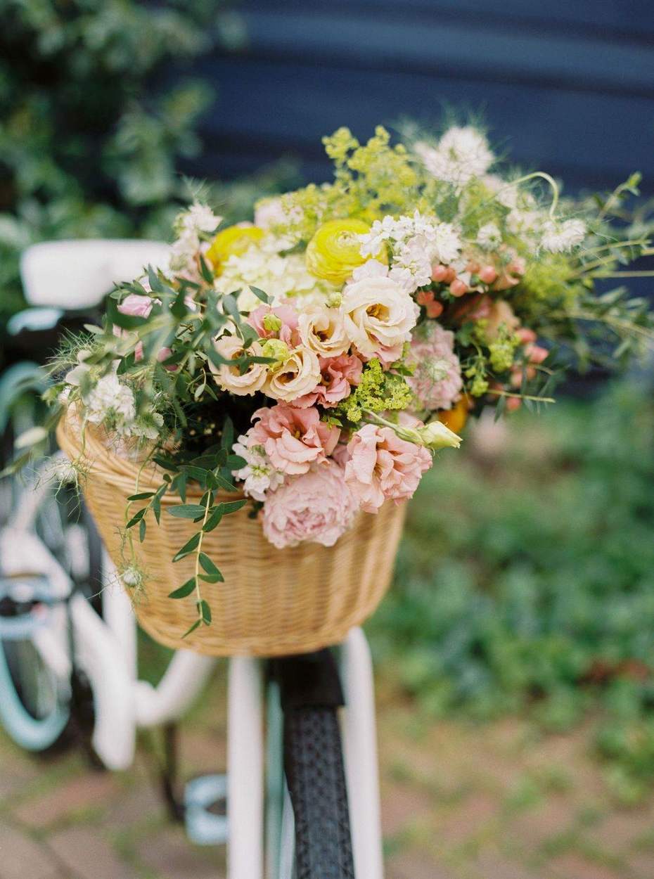 Wicker bicycle basket overflowing with pink lisianthus, peony, yellow ranunculus and greenery.