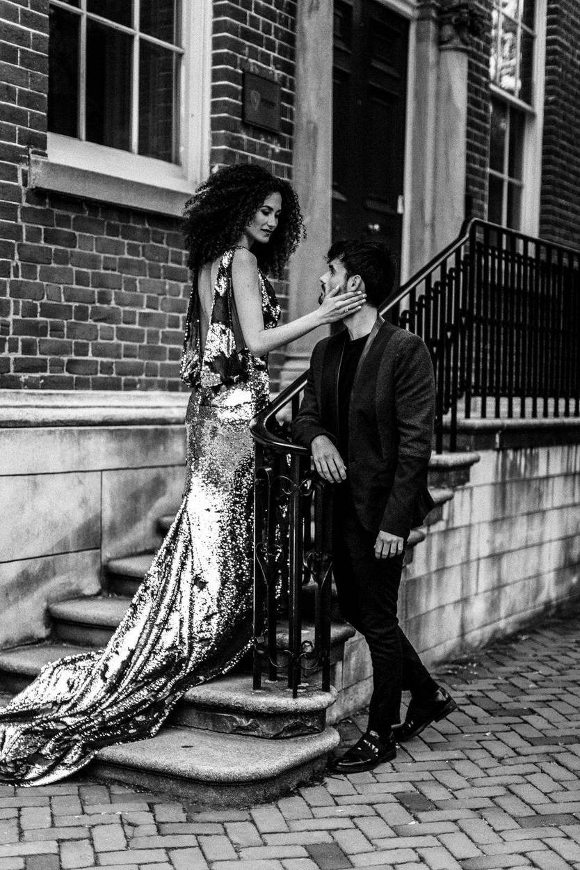 Black-and-white engagement portrait on a historic Old Town Alexandria stoop, her sequin train cascading beside an iron railing.