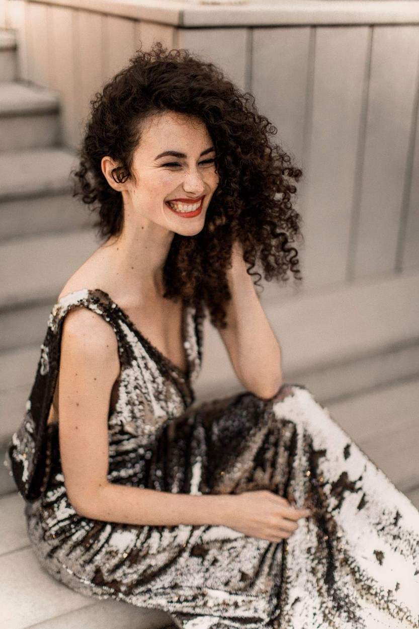 Woman laughing on pale stone steps in a sequin gown, a candid Old Town Alexandria engagement portrait.