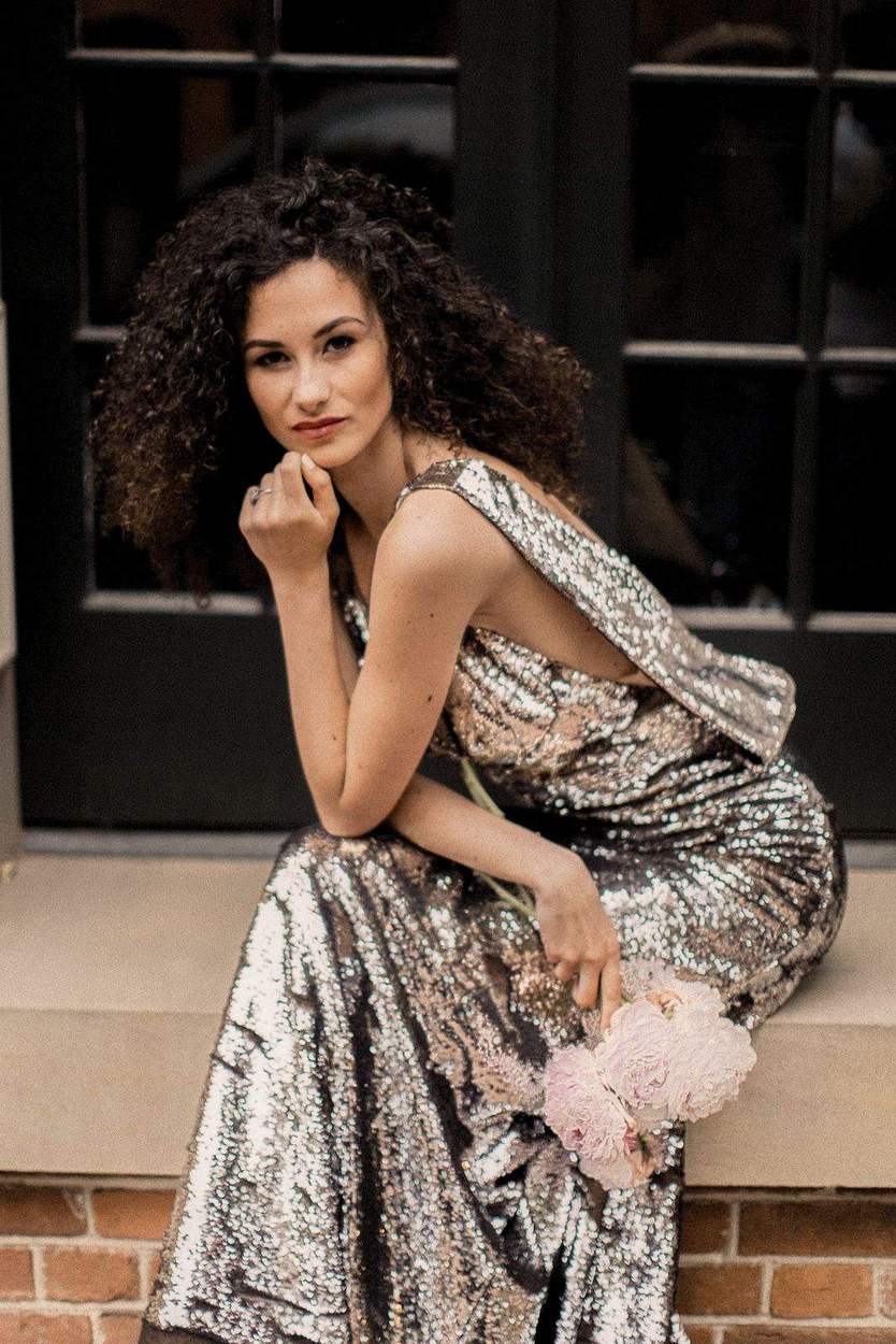 Woman in a sequin gown holding pale pink peonies on a stone window ledge, an Alexandria VA engagement portrait.