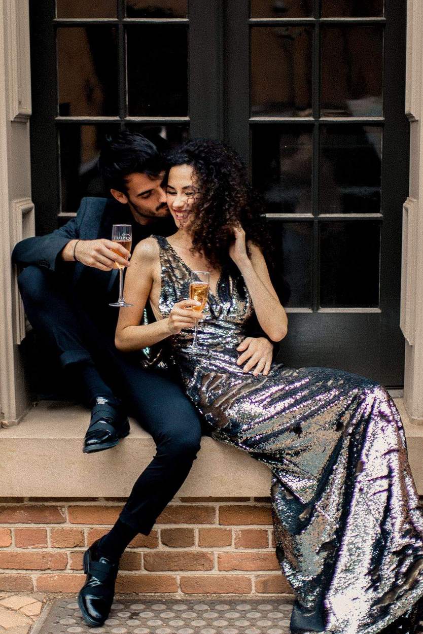 Couple sharing champagne on a stone window ledge beside black French doors and red brick in Old Town Alexandria.