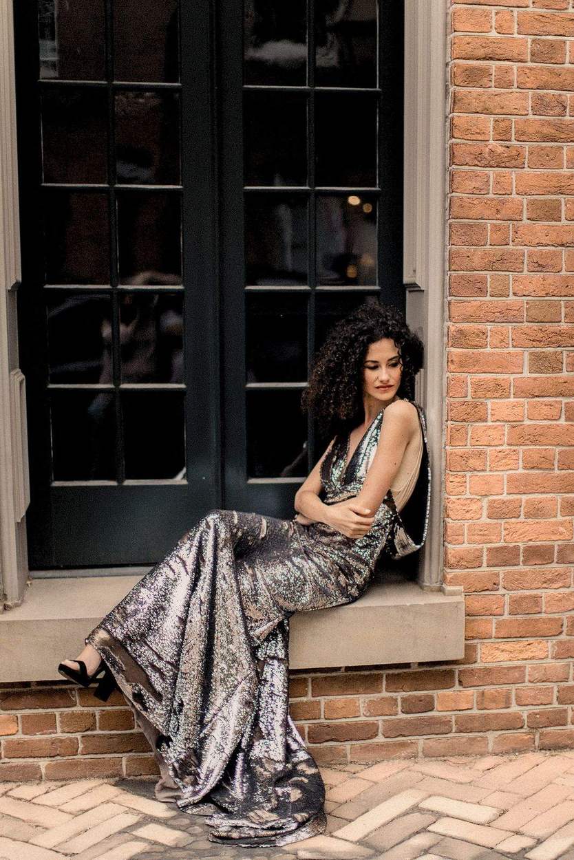 Woman in a sequin gown seated on a stone window ledge against red brick in historic Old Town Alexandria, Virginia.