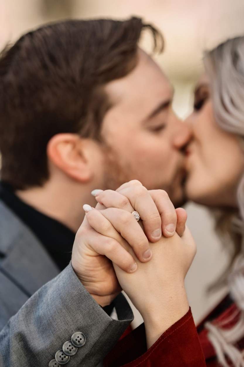 Close kiss with the couple's hands clasped together and an engagement ring catching the light.