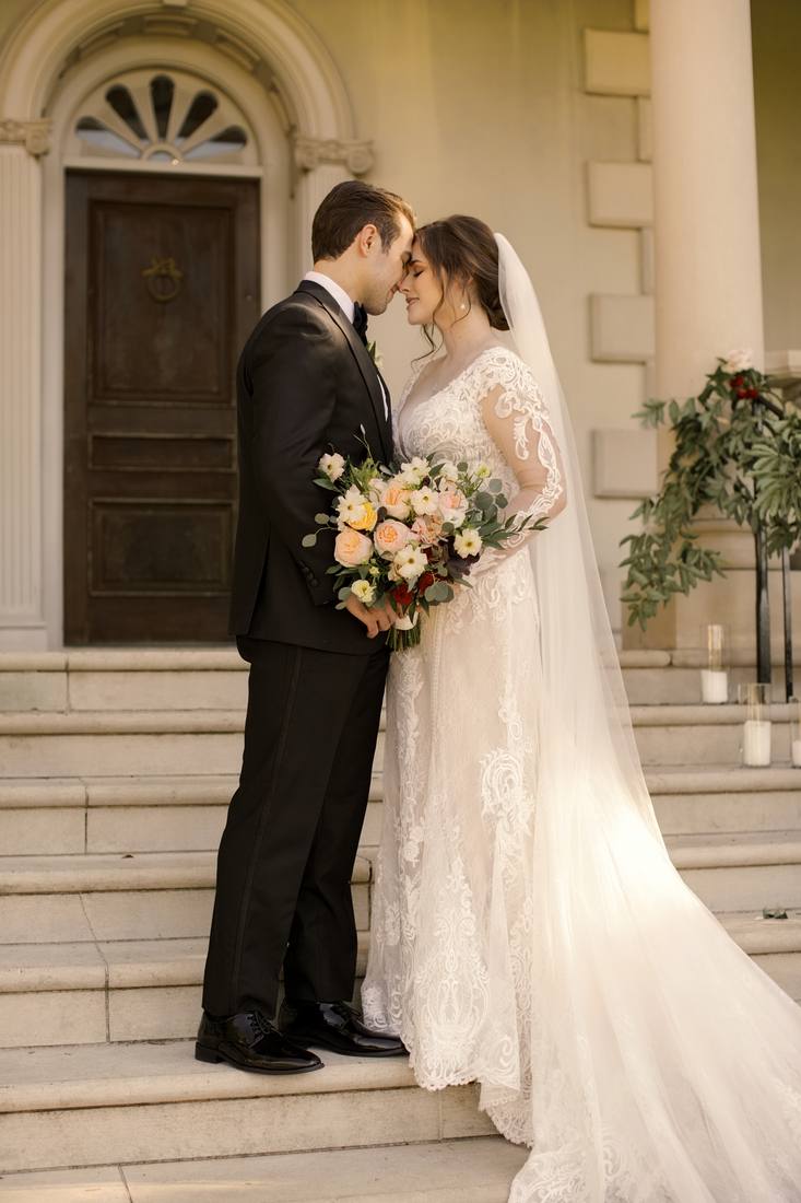 Bride and groom standing forehead to forehead on the mansion steps beneath an arched doorway with a fan window