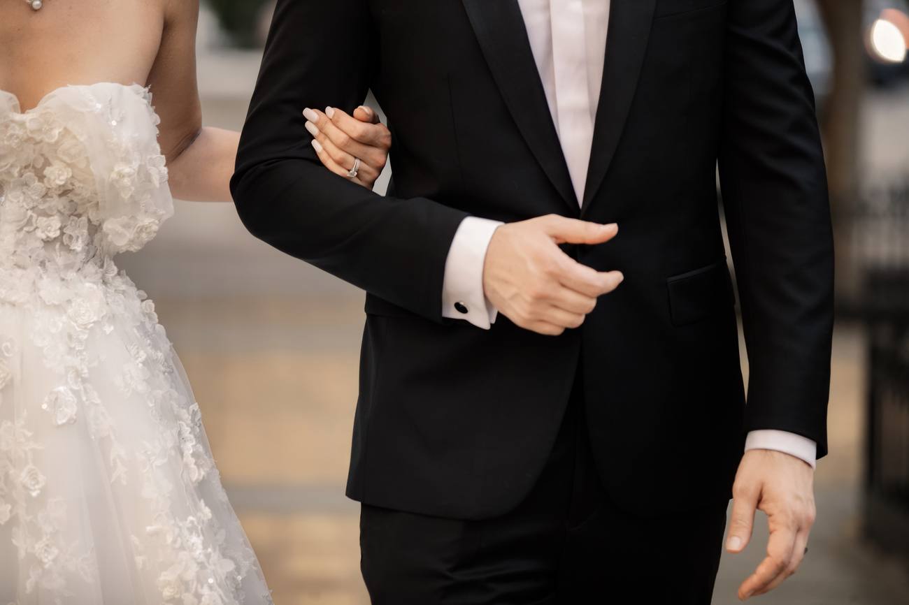 Detail of the bride's hand with her ring resting on the groom's arm, beside his tuxedo cuff and cufflink