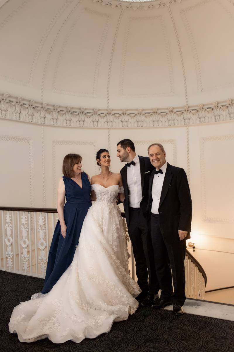 Bride standing with a woman in a blue gown and two men in black tie beneath a domed ceiling