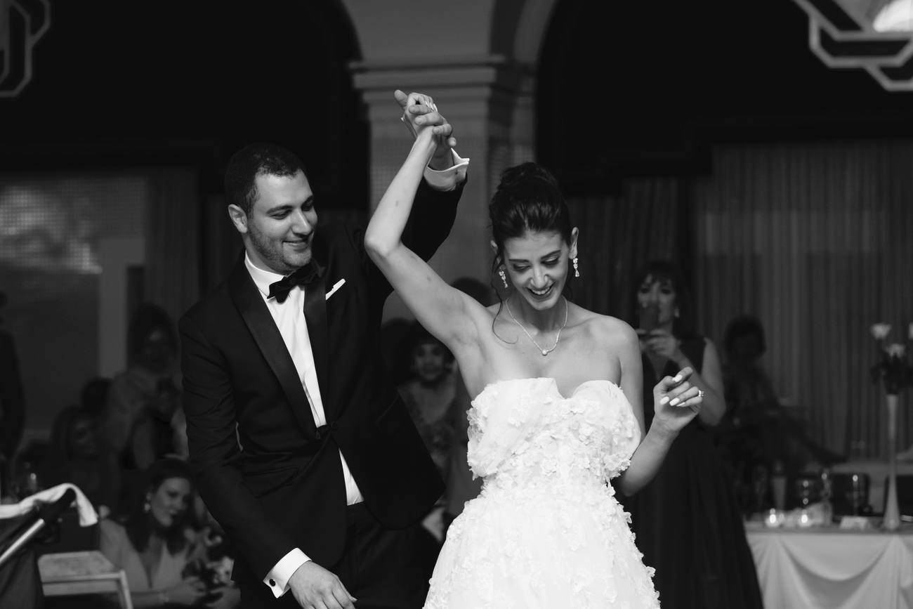 Black and white photo of the groom twirling the bride, her arm raised, as they dance in the ballroom