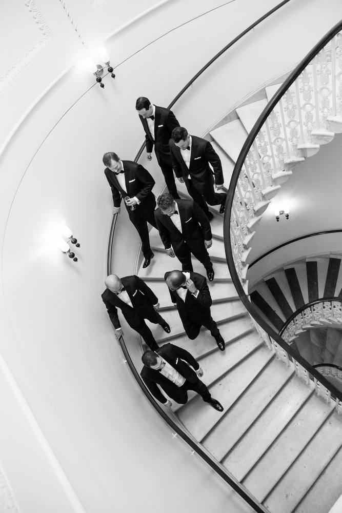Overhead view of men in black tuxedos on a white spiral marble staircase