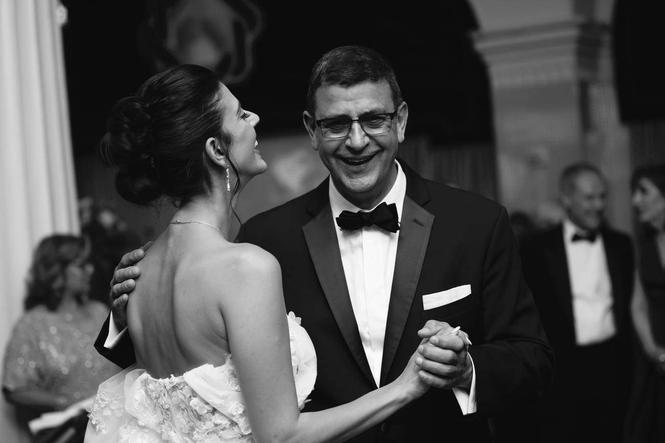 Black and white photo of the bride dancing and laughing with a smiling man in black tie