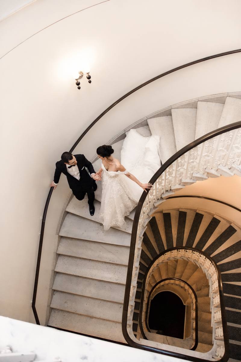 View from above of a bride and groom descending a spiral marble staircase hand in hand