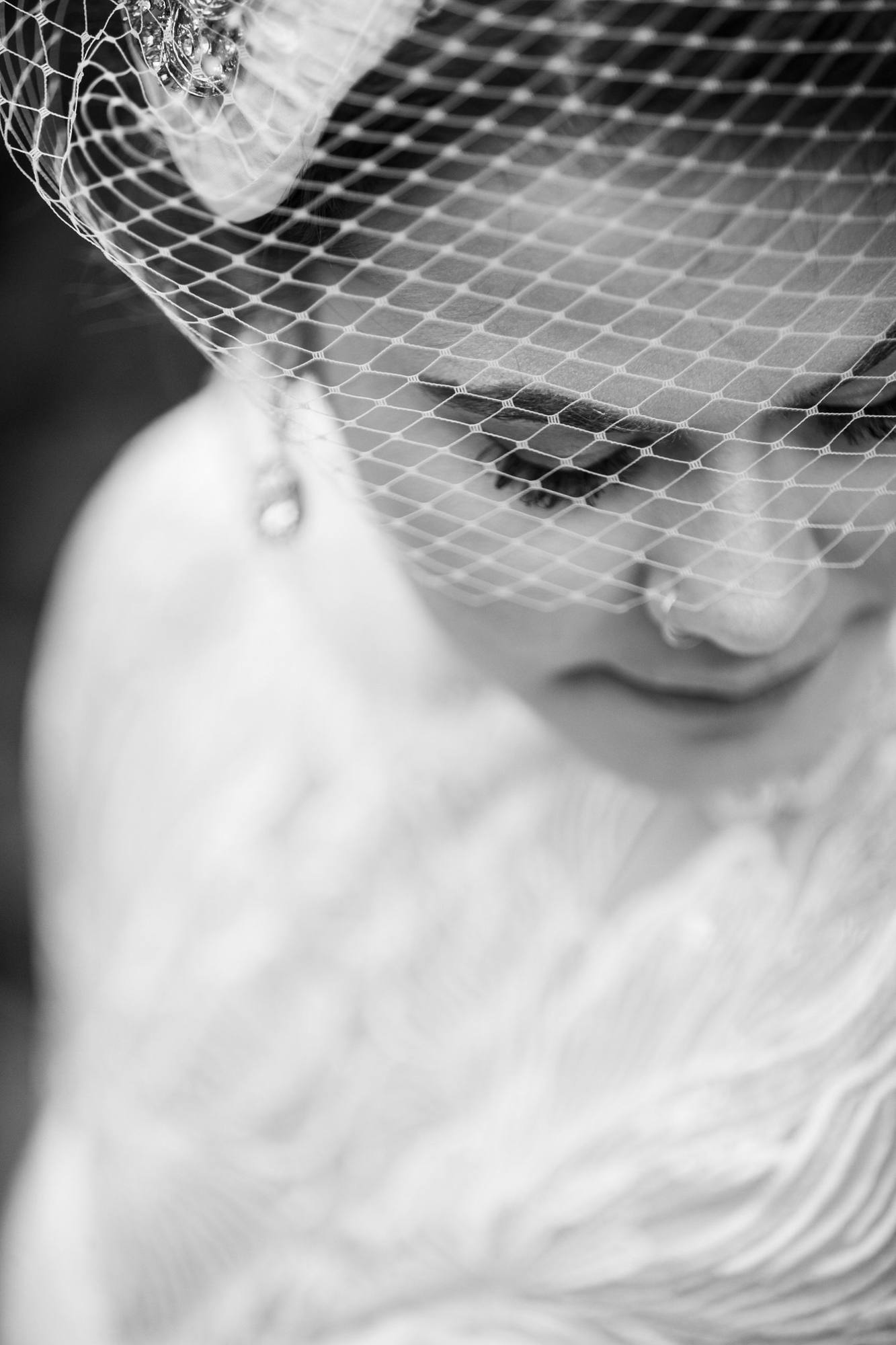 Black and white close portrait of the bride looking down through a birdcage veil