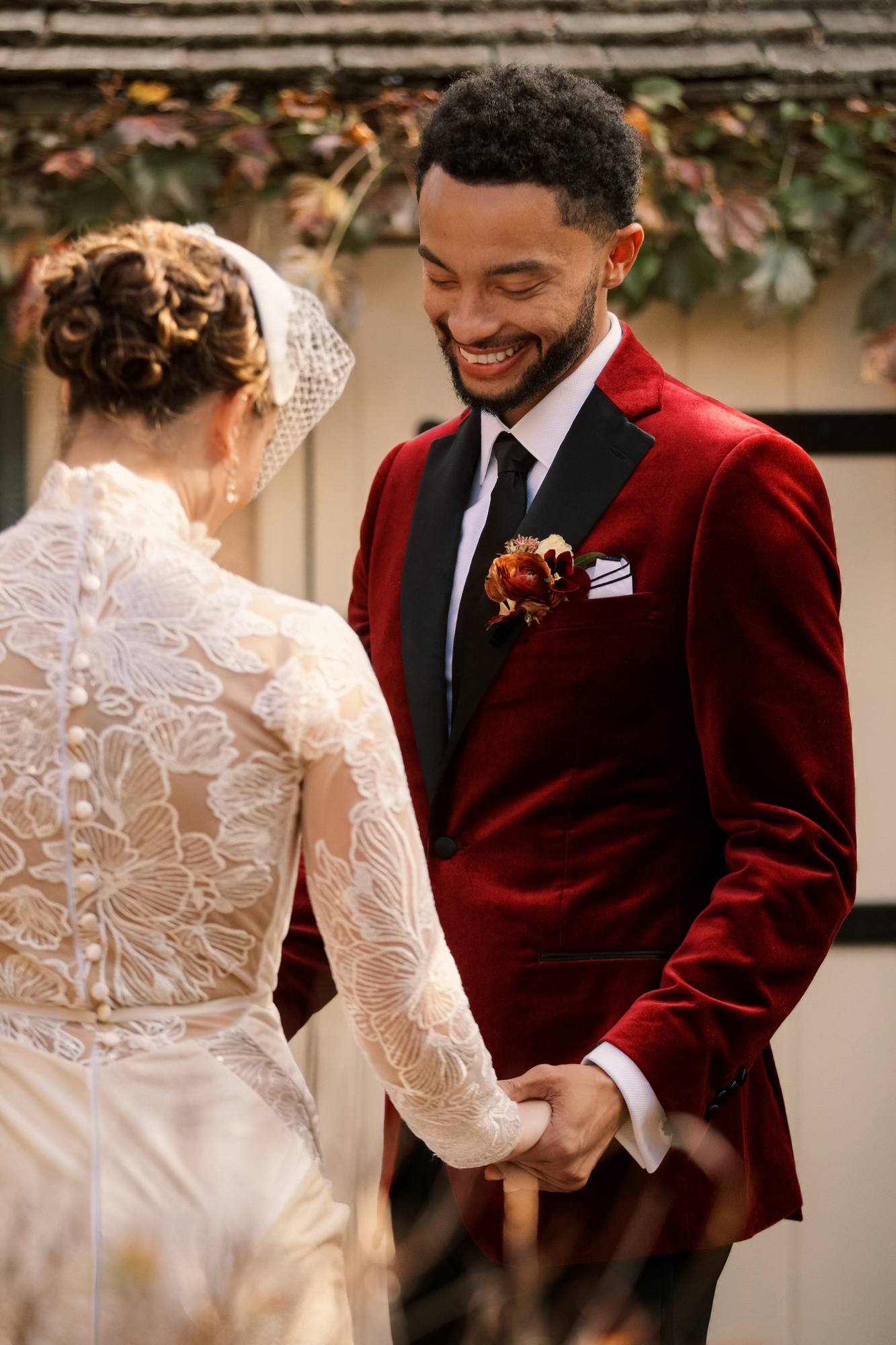 Groom smiling down at the bride as they hold hands at their first look, her lace back with a row of covered buttons toward the camera