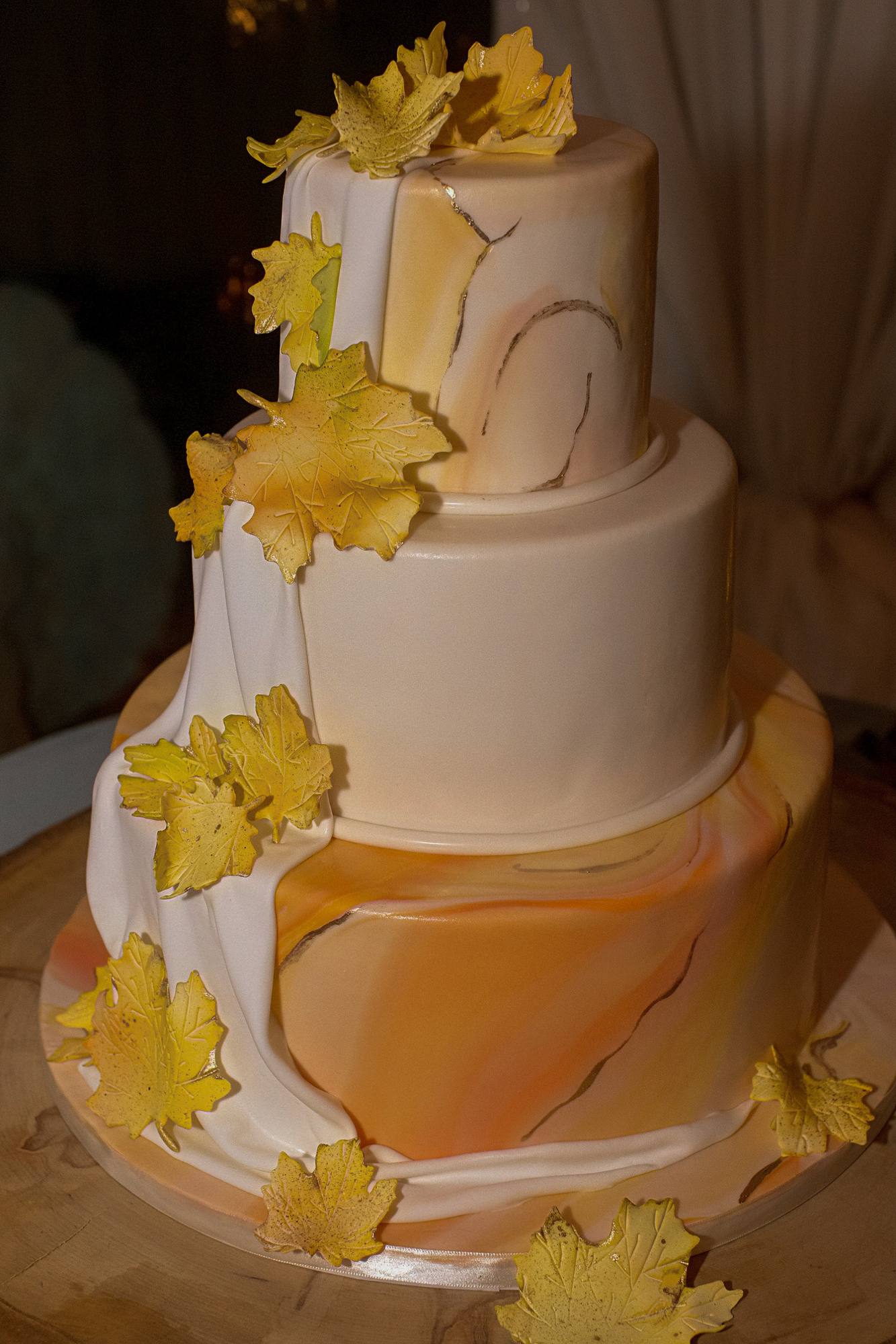 Three-tier wedding cake with marbled orange and gold fondant and sugar maple leaves on a wood slab