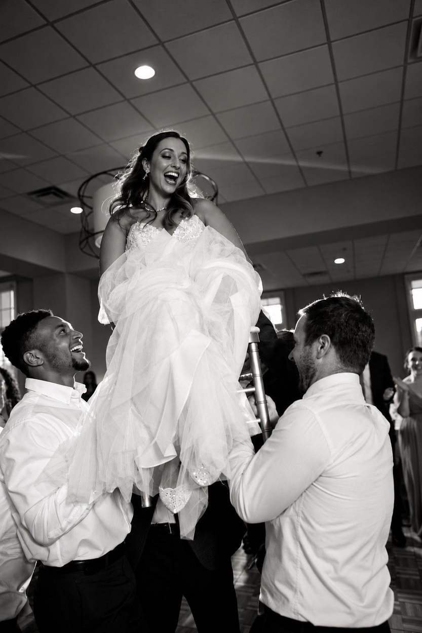 Washington DC photographer wedding reception photo: a joyful bride laughing as guests lift her high on a chair.
