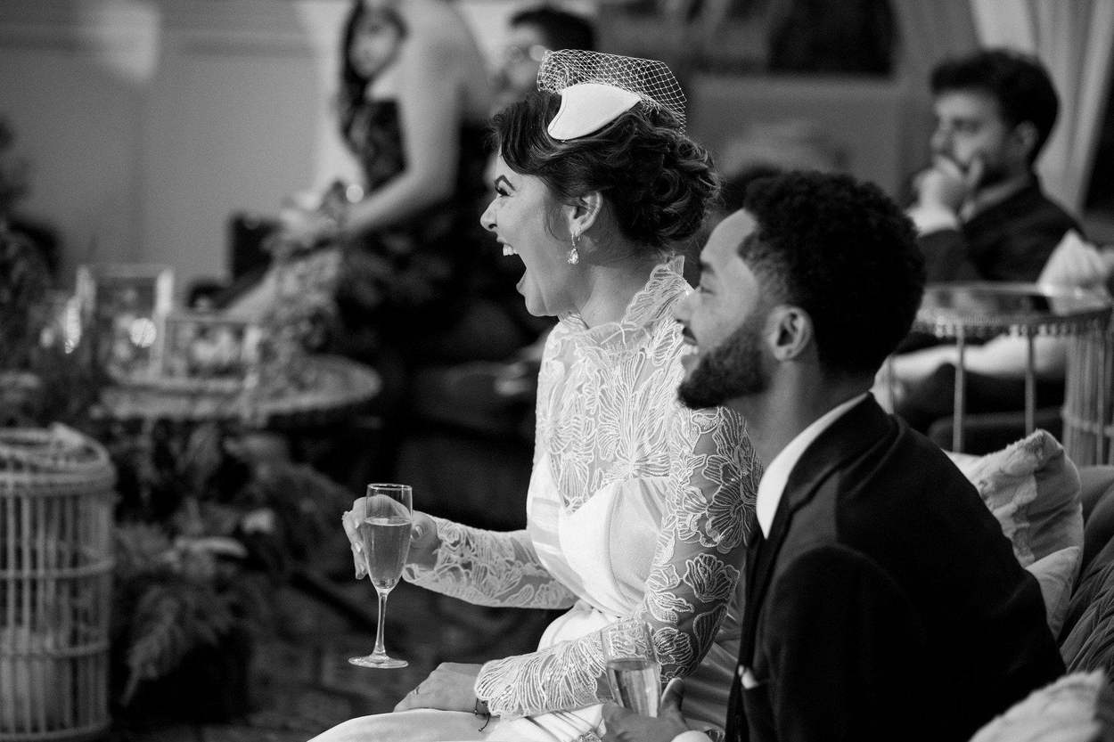 Washington DC photographer black and white wedding photo: a bride in a lace gown and birdcage veil and her groom laughing together with champagne.